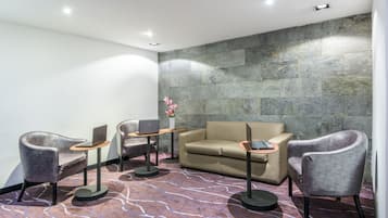 A modern lounge area with a beige sofa, two grey armchairs, and a small table with a laptop.