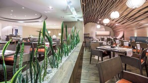 Un comedor moderno con mesas largas, sillas y una jardinera central con plantas verdes.