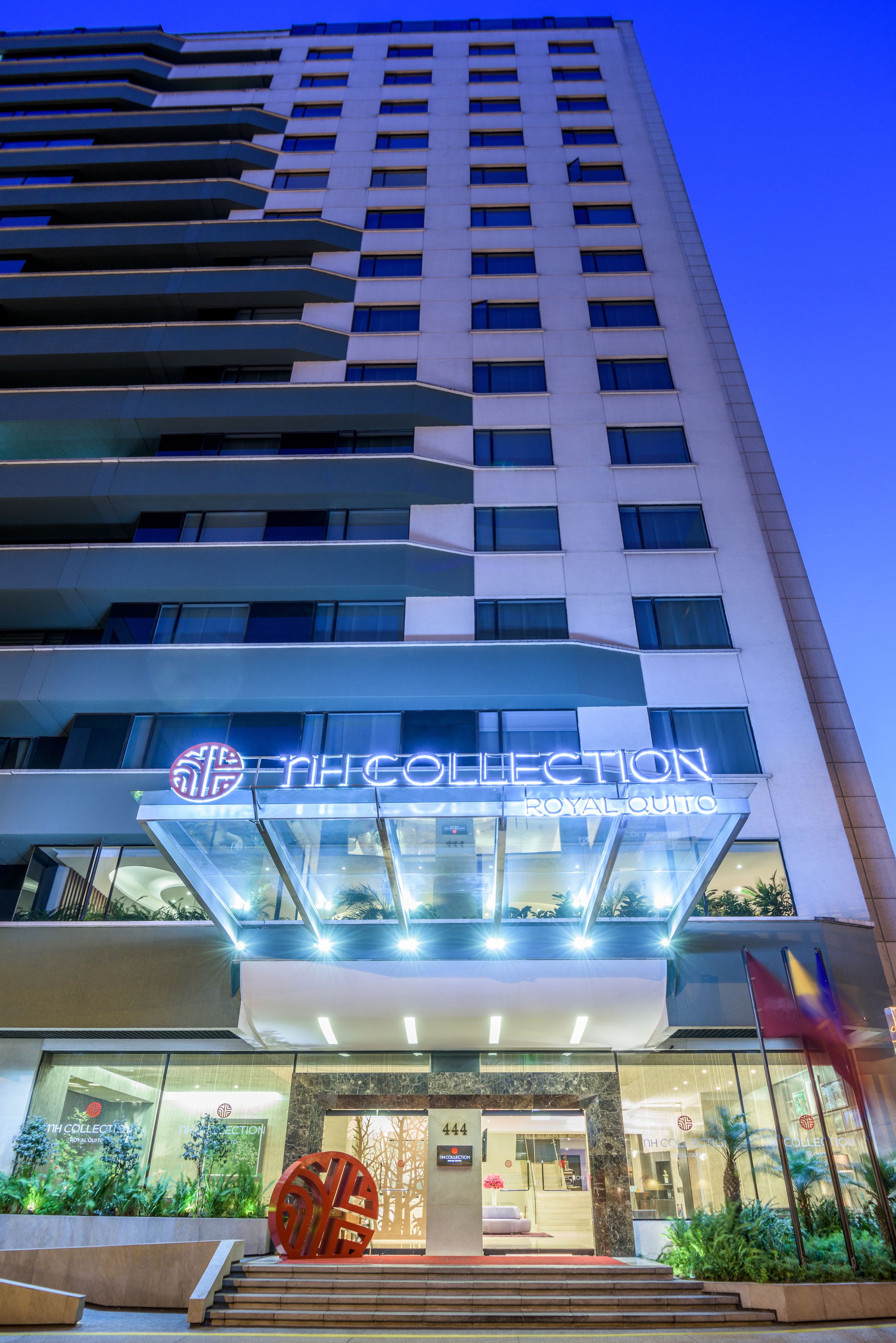A hotel entrance with a modern design, featuring a glass facade and a prominent sign for "The Collection Royal Quinto".