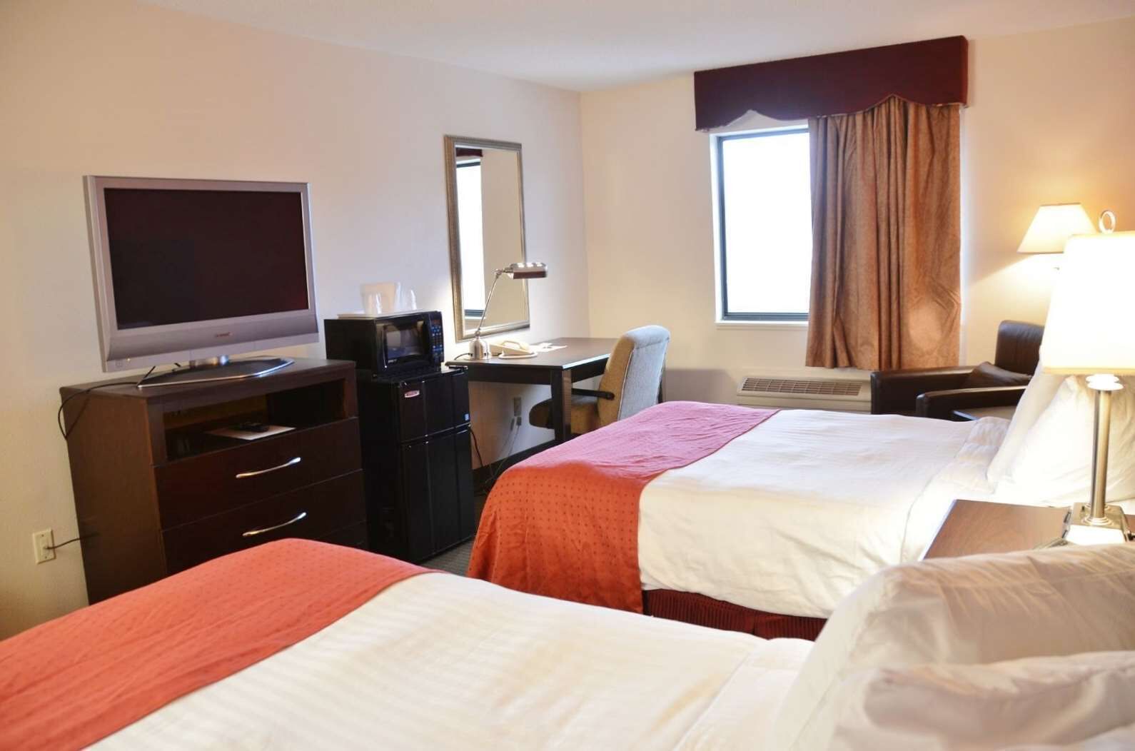 A hotel room with two beds, a desk with a computer, a television, a microwave, and a window with curtains.