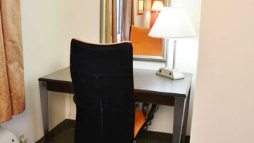 A hotel room with a desk, a chair, a lamp, and a mirror.