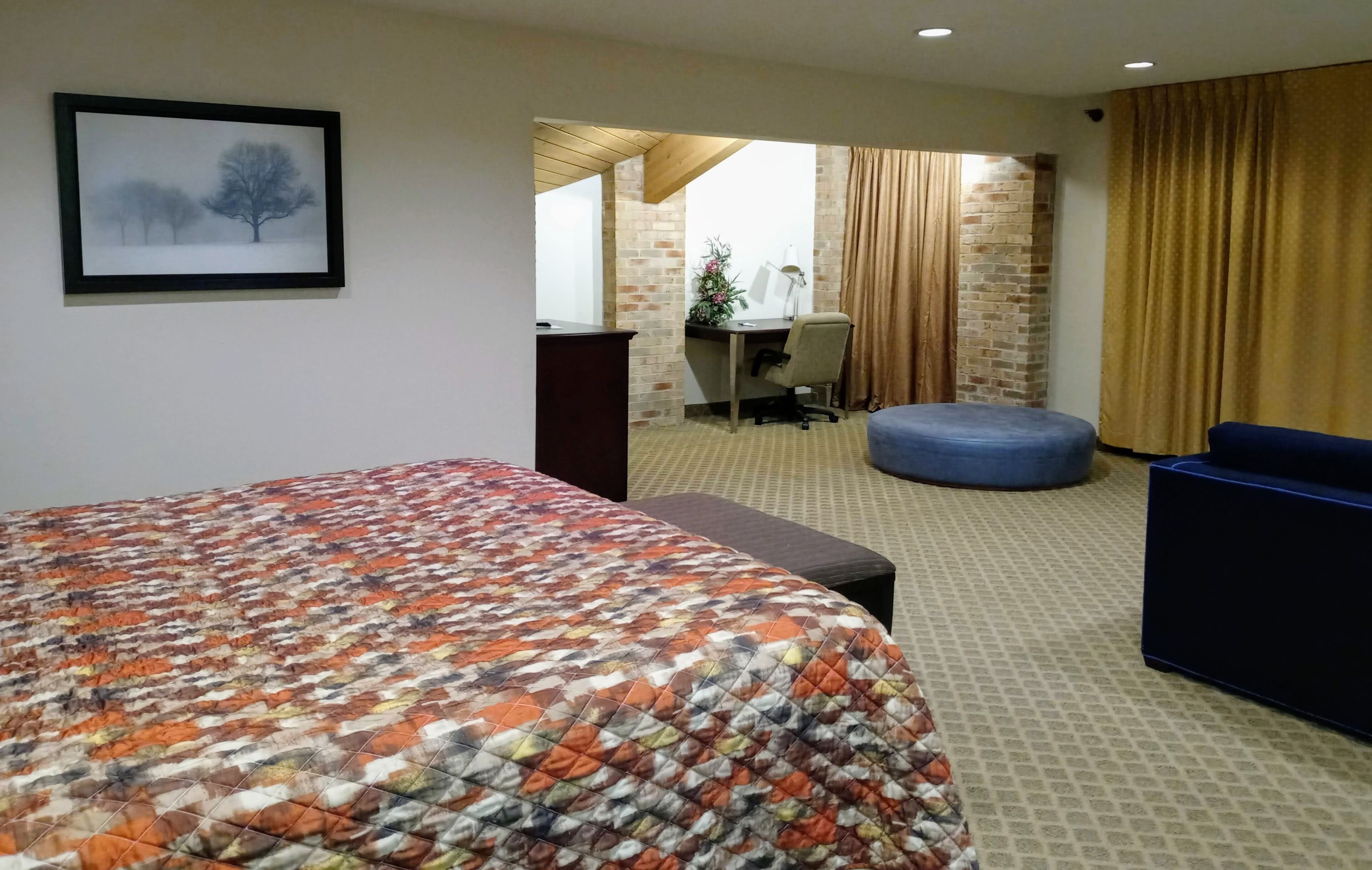 Une chambre d’hôtel avec un grand lit, un bureau, une chaise et un pouf bleu.