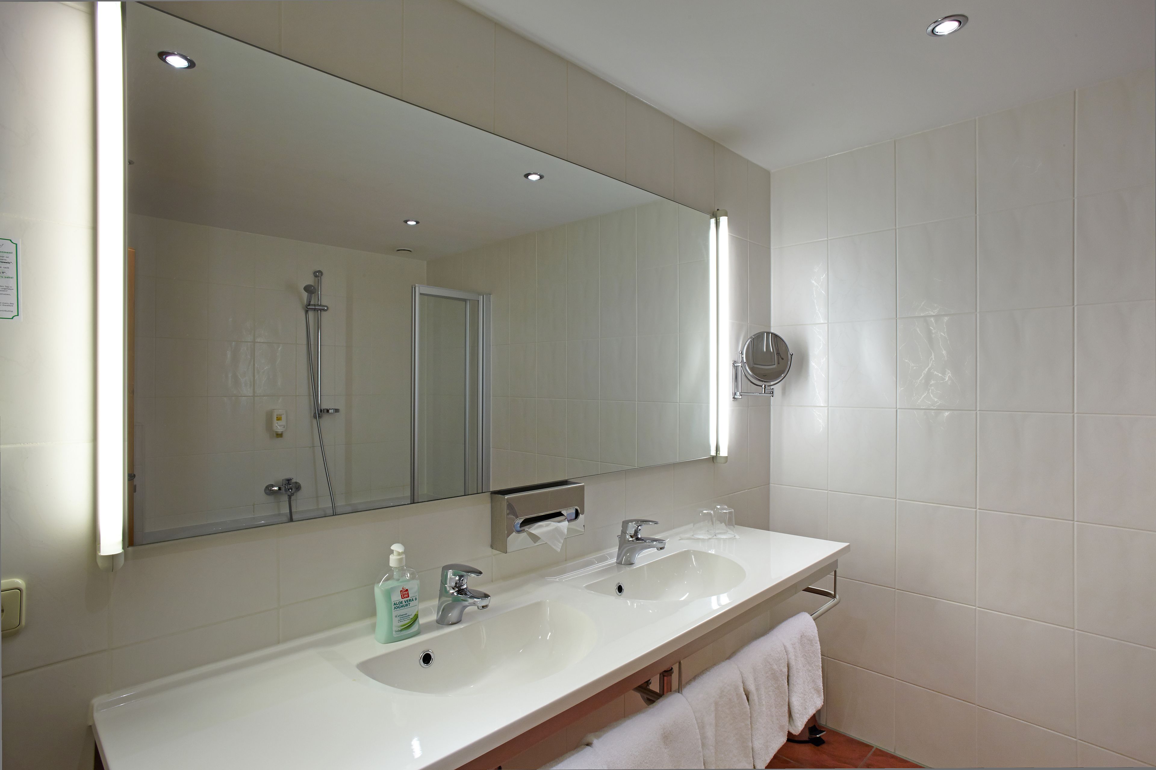 Un baño moderno con dos lavamanos, un espejo grande y una ducha.