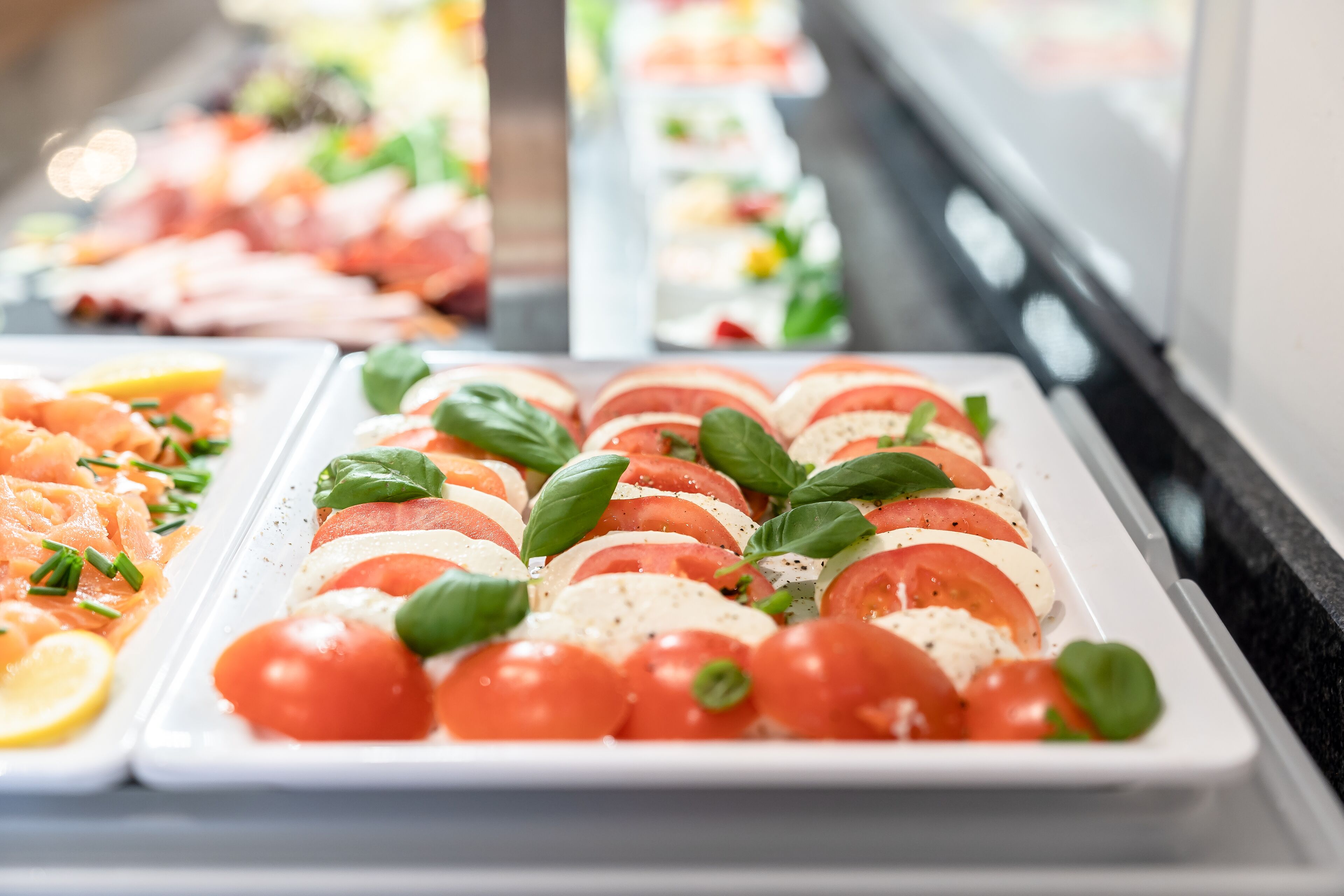 A buffet with various food options including a dish with tomatoes, basil, and cheese.