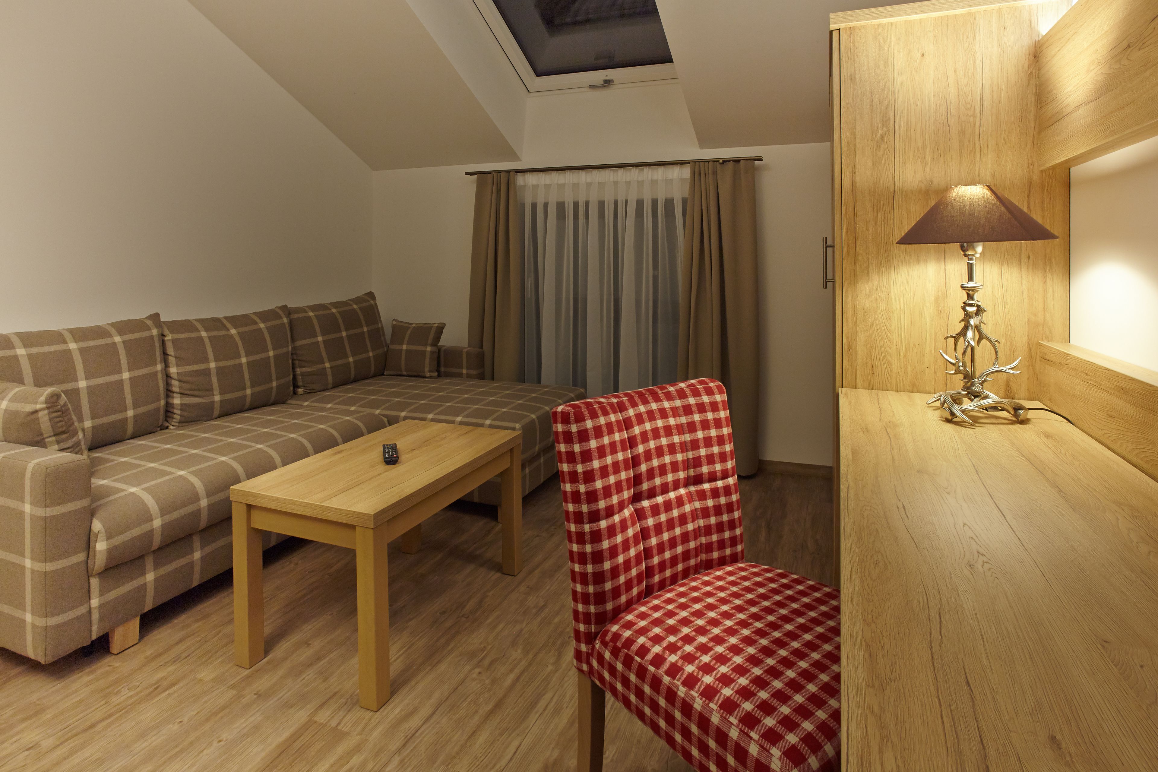 Una sala de estar acogedora con un sofá, un sillón a cuadros rojo y blanco, una mesa de centro de madera y una lámpara sobre una mesita auxiliar de madera.