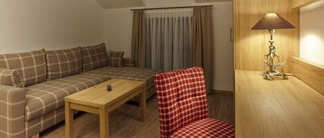 Una sala de estar acogedora con un sofá, un sillón a cuadros rojo y blanco, una mesa de centro de madera y una lámpara sobre una mesita auxiliar de madera.