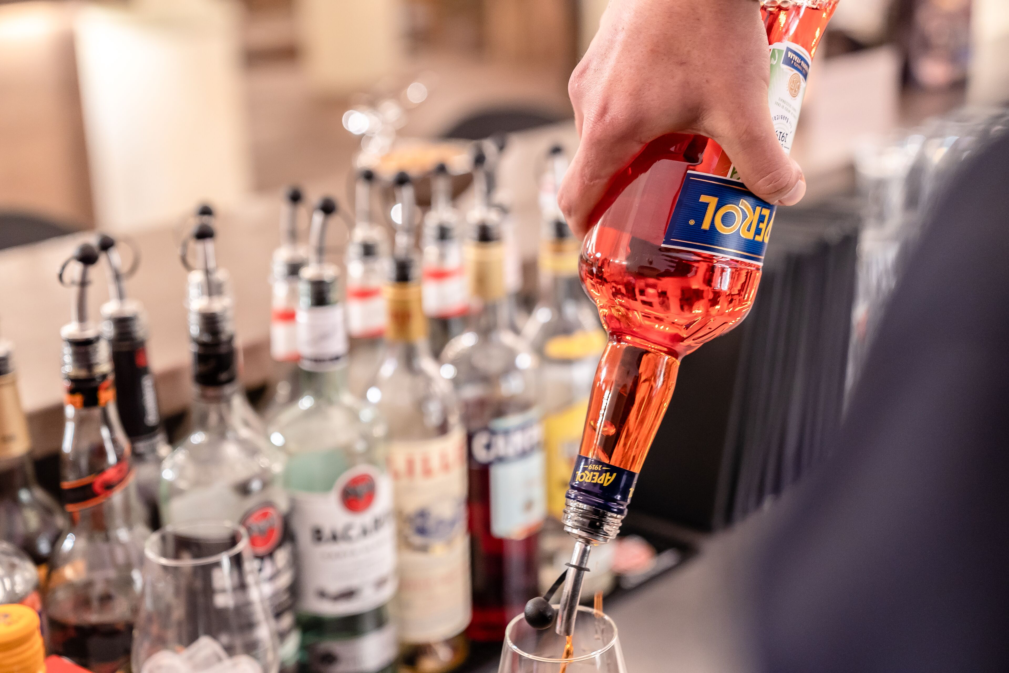 A hand pouring a red liquid from a bottle into a glass.