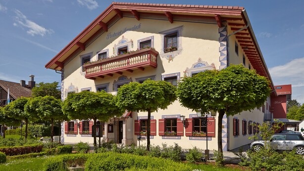 A traditional building with a balcony, red shutters, and a garden in front. - Hotel Sauerlacher Post (Sauerlach)