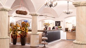 A lobby with marble columns, a reception desk, and a chandelier. - Hotel Sauerlacher Post (Sauerlach)