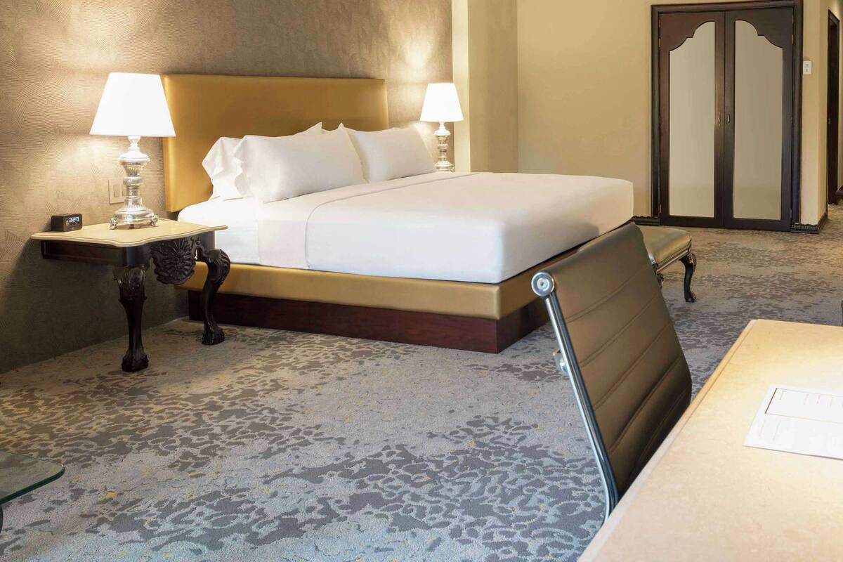 Een hotelkamer met een bed, twee bedlampen, een nachtkastje, een bureau en een garderobe.