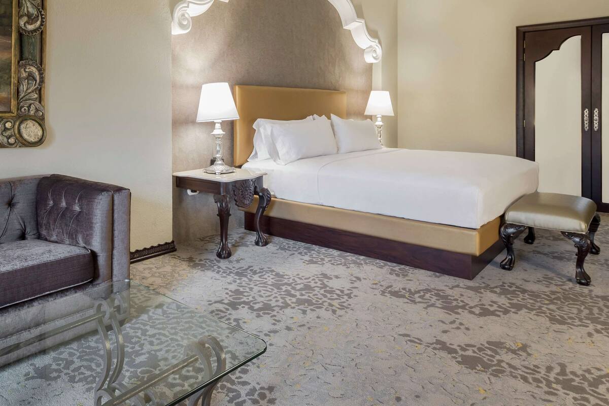 Een hotelkamer met een groot bed, twee bedlampen, een stoel en een glazen tafel.