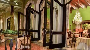 An interior with open doors leading to a dining area, wooden chairs, and a chandelier.