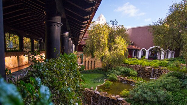 A garden with a pond, stone structures, and a building with a dome in the background.