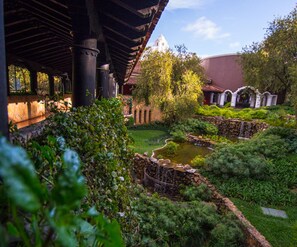 A garden with a pond, stone structures, and a building with a dome in the background. - Hilton Guatemala City (Santa Catarina Pinula)