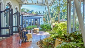 A covered outdoor dining area with tables and chairs, surrounded by lush greenery and a view of the landscape.