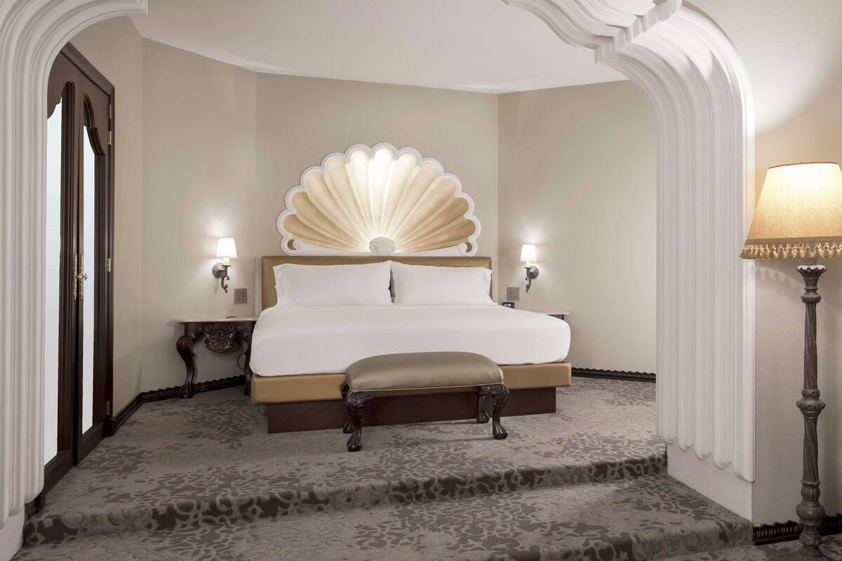 Een slaapkamer met een groot bed, twee nachtkastjes, een bankje en een lamp.