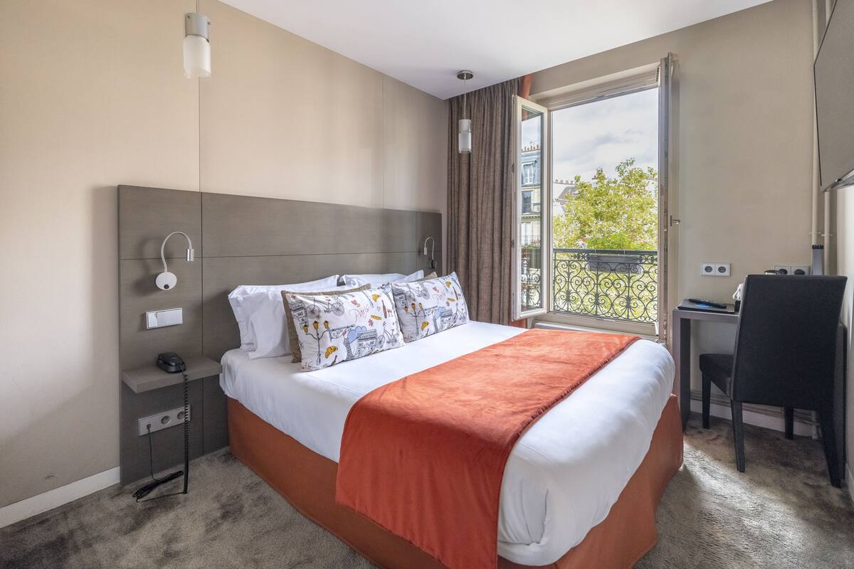 A hotel room with a bed, bedside table, and a desk with a chair.