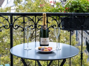 Una mesa con una botella de champán, dos copas y un plato de macarons en un balcón.
