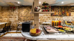 A buffet with a variety of food items, a marble countertop, and a stone wall with a mural. - Hôtel Minerve Paris (Paris)
