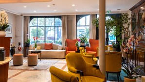 A hotel lobby with a sofa, yellow armchairs, a coffee table, and a large window offering a view of the street. - Hôtel Minerve Paris (Paris)