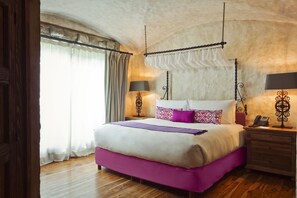 Un dormitorio con una cama grande, suelo de madera, dos lámparas de noche y un dosel sobre la cama.