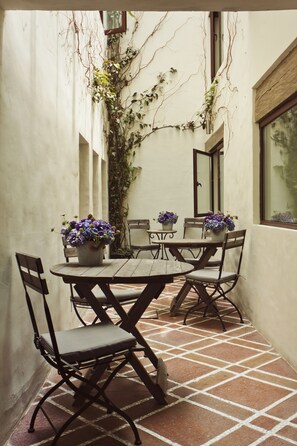 Un patio con una mesa redonda y cuatro sillas, rodeado de plantas en macetas y enredaderas.