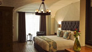 Un dormitorio amplio con una cama grande, una araña de techo, un jarrón con flores y vistas al exterior.