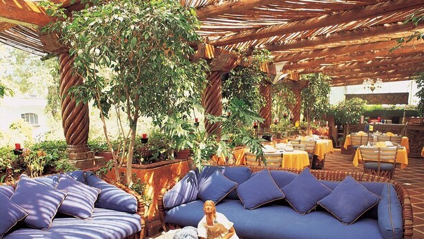 Un espacio al aire libre acogedor con sofás azules acolchados y una mesa central con una escultura decorativa.