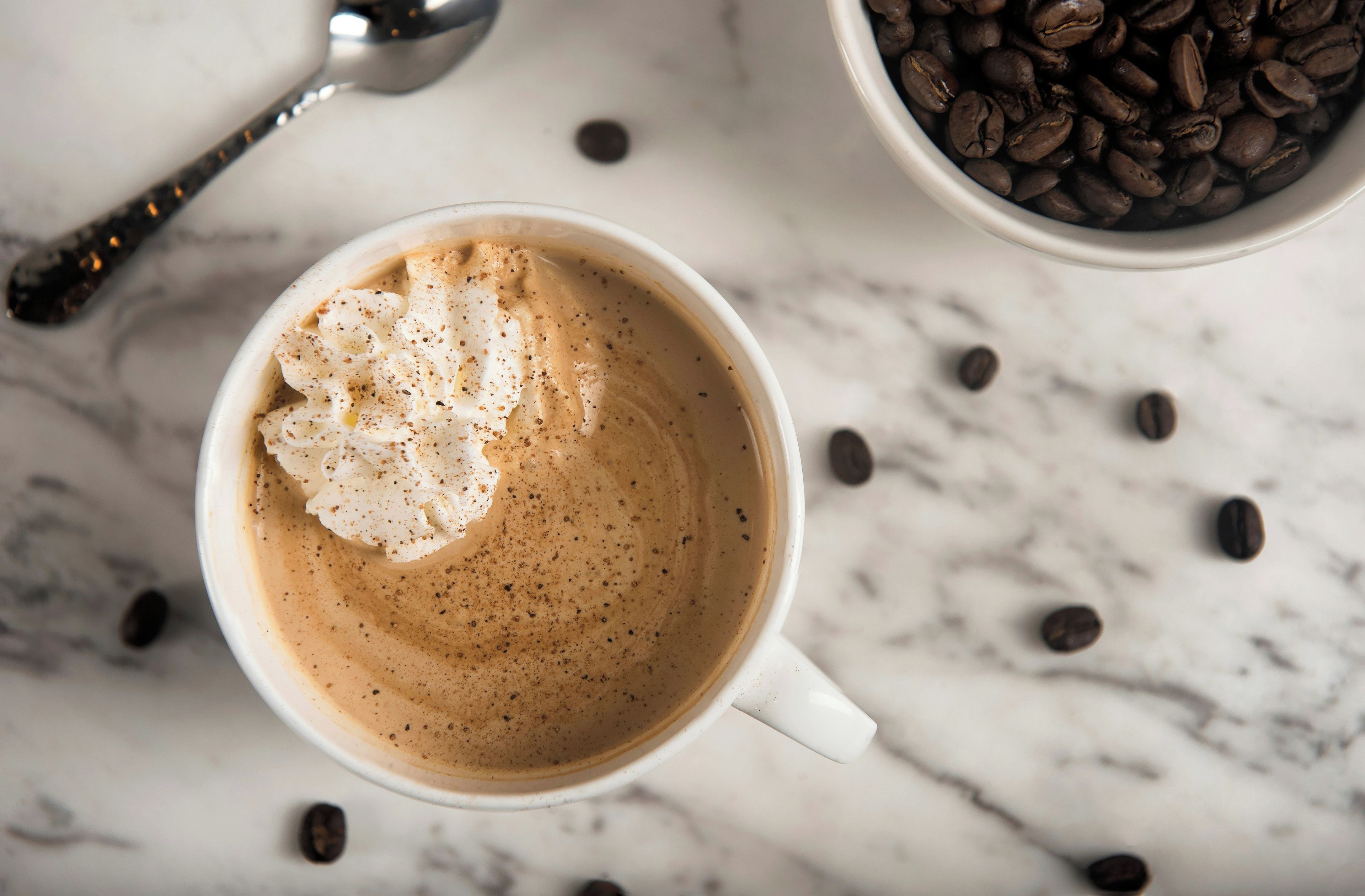 A white cup of coffee with a dollop of whipped cream on a marble surface.