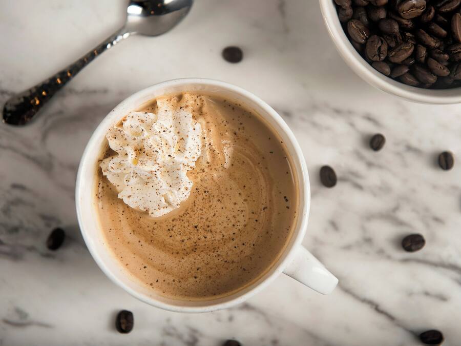 A white cup of coffee with a dollop of whipped cream on a marble surface.