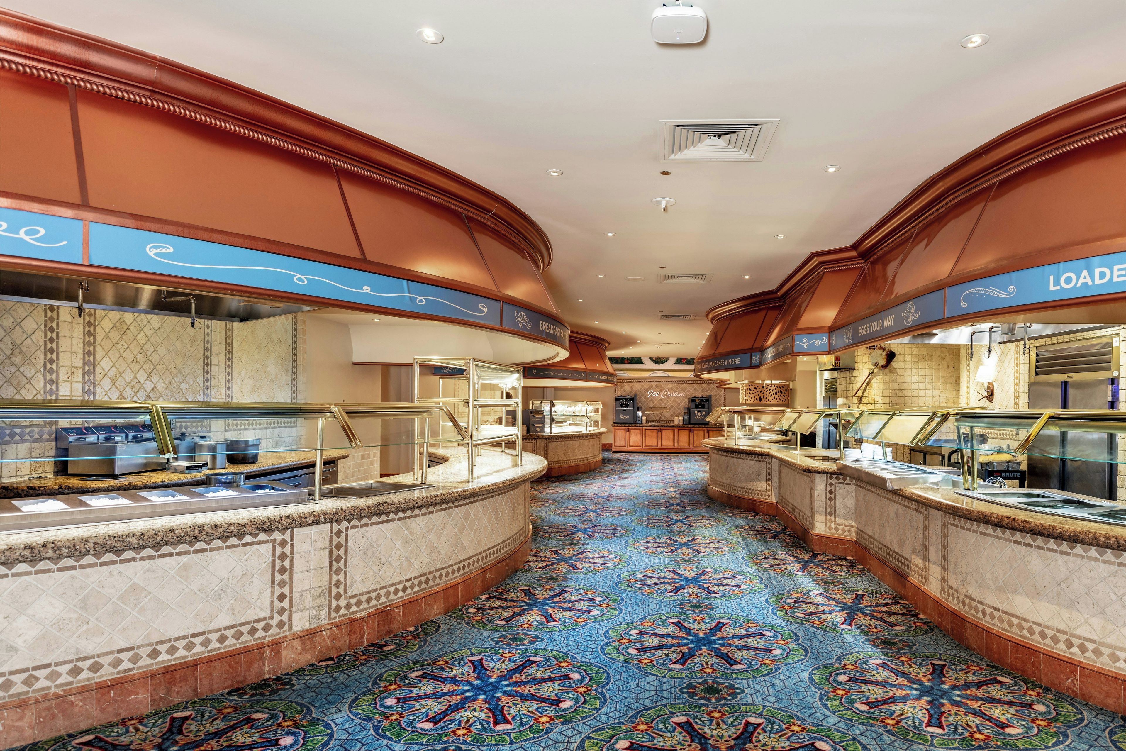 A hotel lobby with a central walkway, buffet counters, and a patterned carpet.