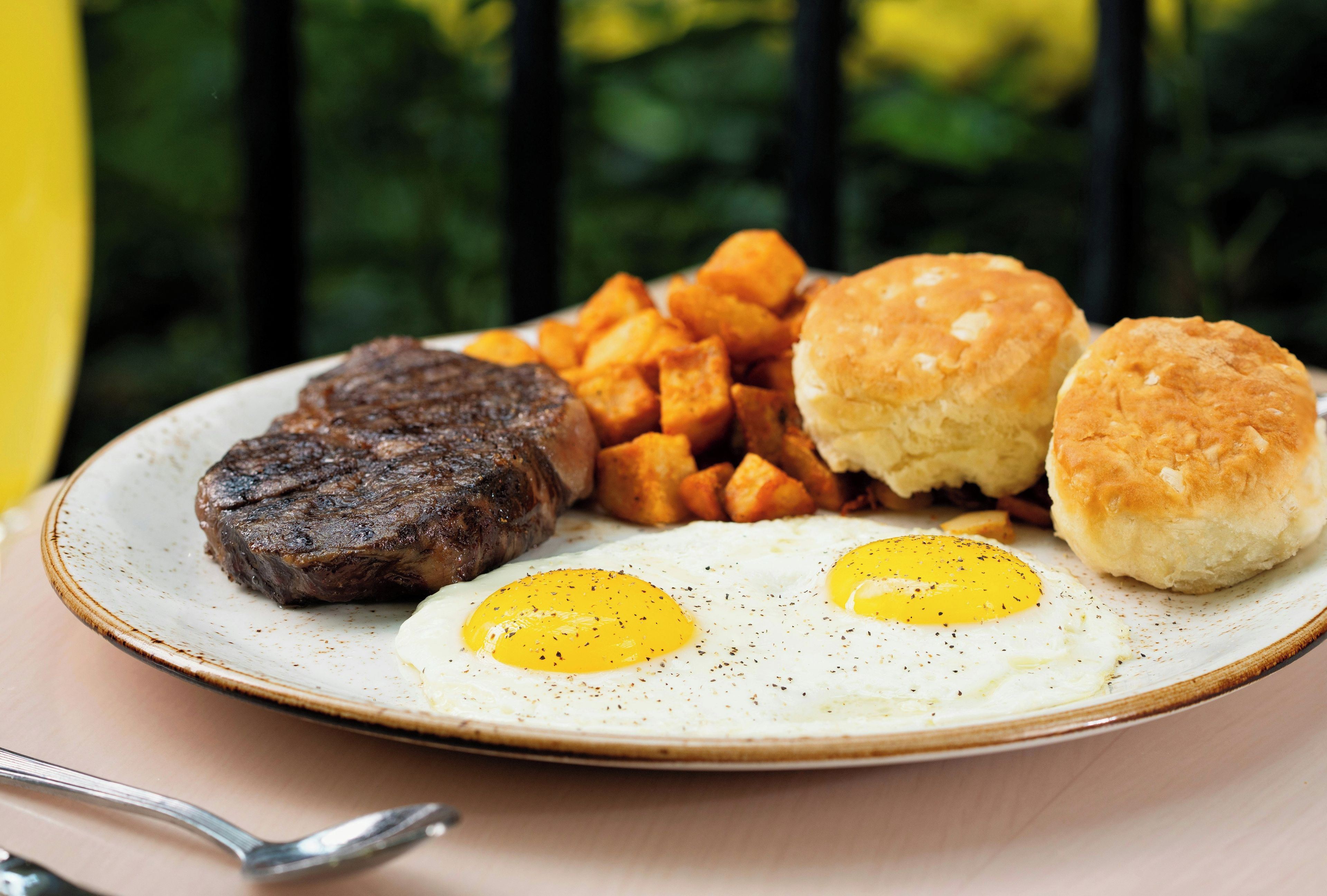 A plate with a steak, fried eggs, biscuits, and roasted potatoes.