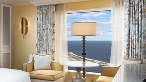 A hotel room with a bed, two armchairs, a table with a lamp, and a window with a view of the ocean. - Beau Rivage (Biloxi)