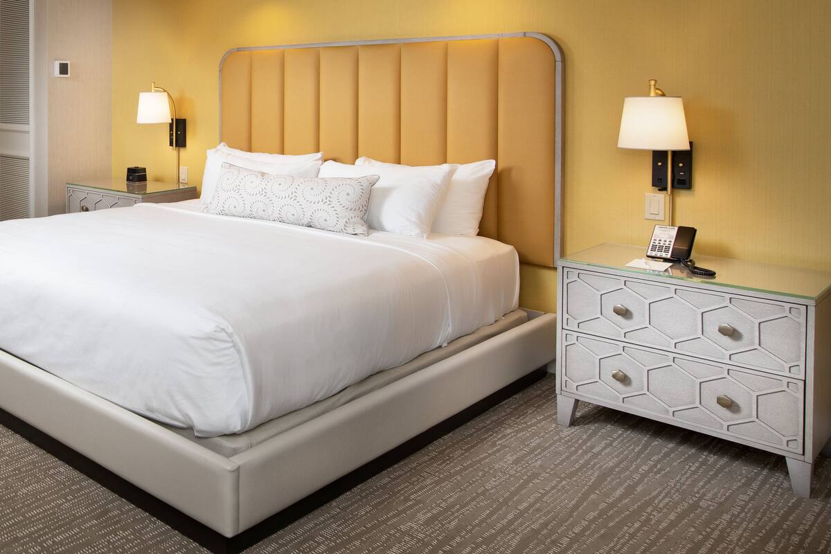 A hotel room with a large bed, two bedside tables, and a nightstand with a lamp.