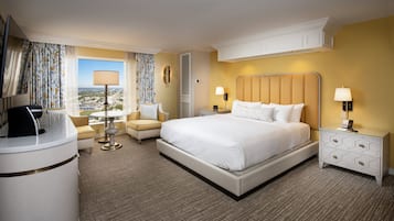 A hotel room with a large bed, a desk with a computer, a chair, a lamp, and a view of the city.