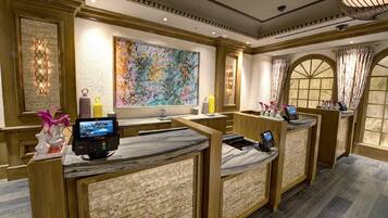 A hotel reception area with marble counters, a large abstract painting, and a view through arched windows.