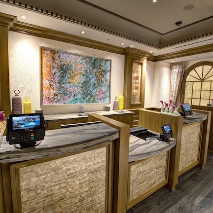 A hotel reception area with marble counters, a large abstract painting, and a view through arched windows.