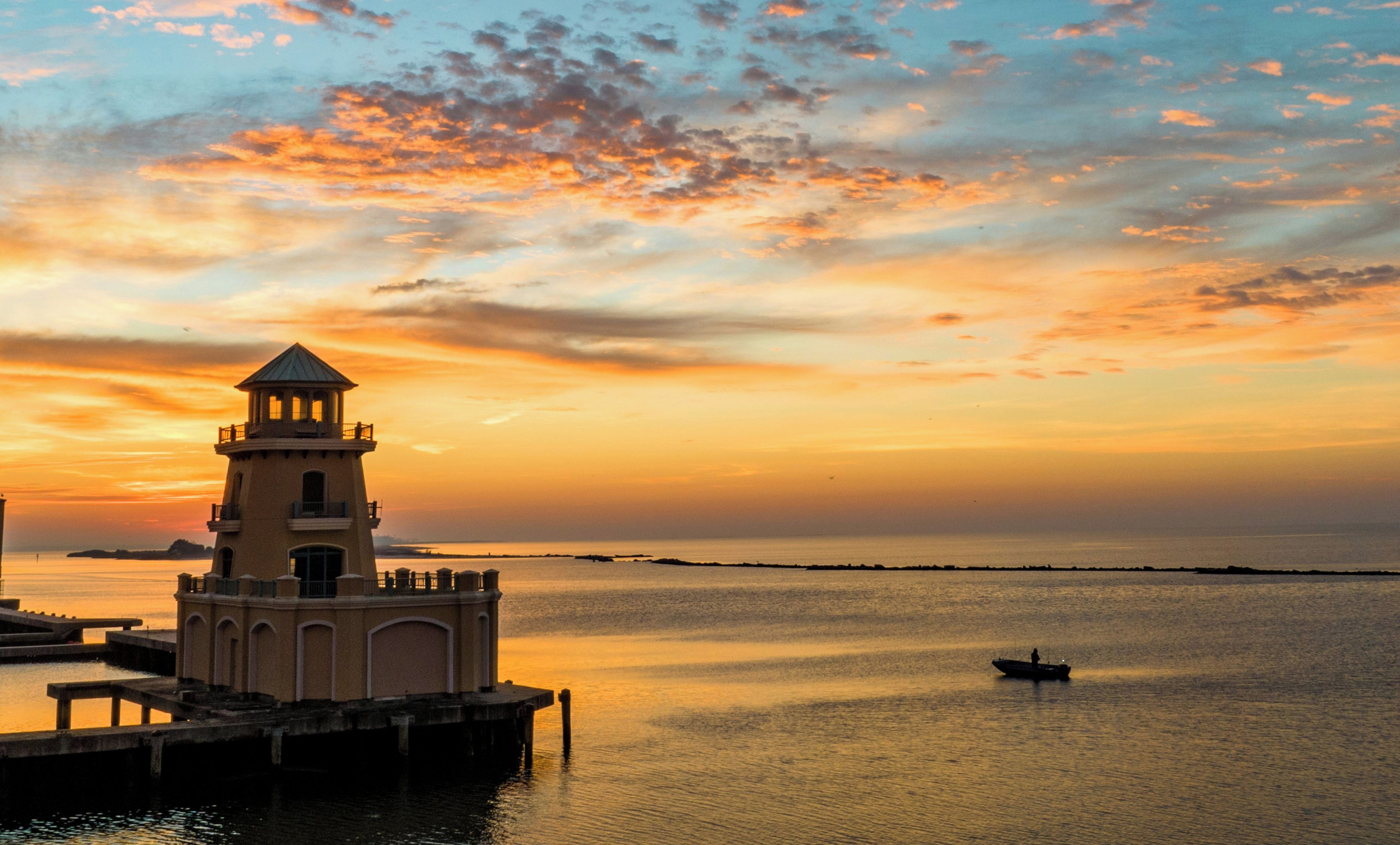 A lighthouse at sunset with calm water and a distant shoreline.