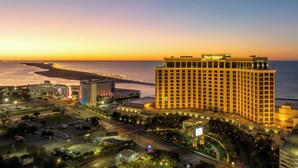 Un hôtel de grande hauteur, reconnaissable à son imposante enseigne « Beau Rivage », situé dans un quartier urbain bien éclairé et offrant une vue sur l’océan au coucher du soleil.