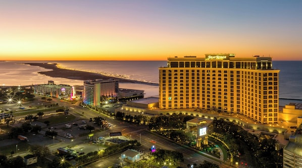 A high-rise hotel with a prominent 'Beau Rivage' sign, surrounded by a well-lit urban area with a view of the ocean at sunset. - Beau Rivage (Biloxi)