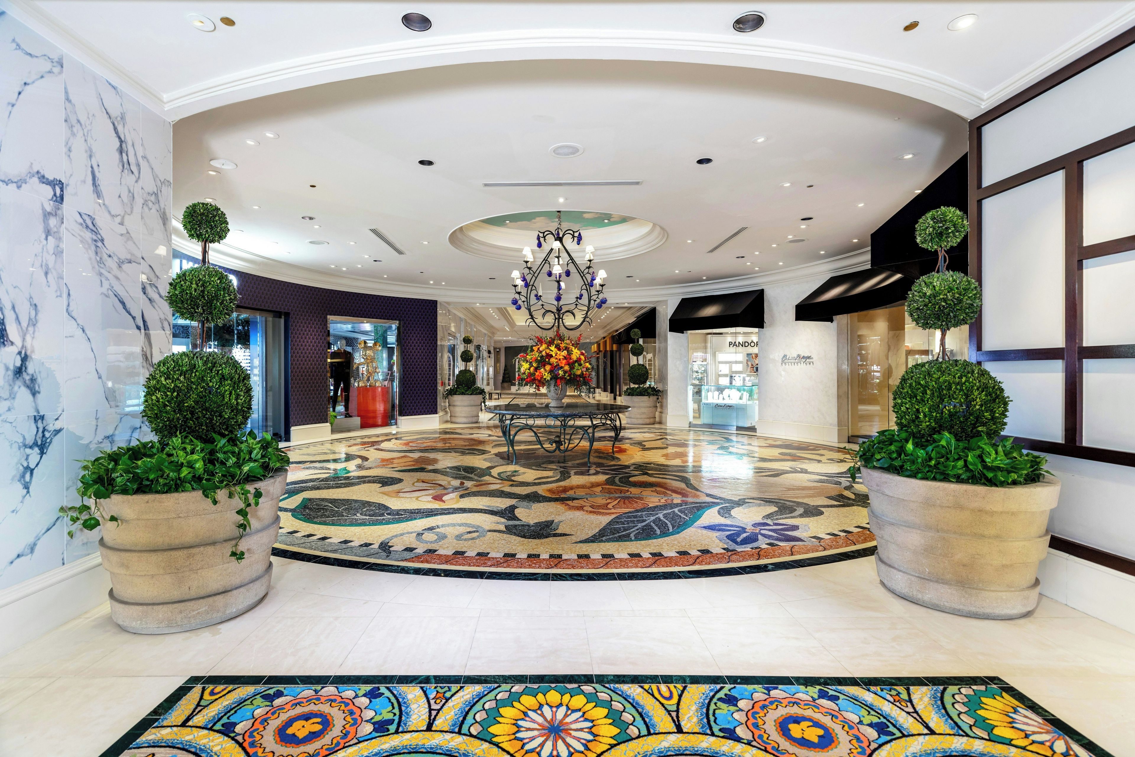 A spacious lobby with a marble floor, a central chandelier, and potted plants.