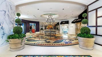 A spacious lobby with a marble floor, a central chandelier, and potted plants.