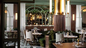 L’intérieur d’un restaurant, avec des tables rondes, des sièges recouverts d’un tissu vert et des lampes suspendues.