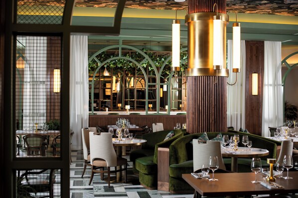 A restaurant interior with round tables, green upholstered seating, and hanging pendant lights.