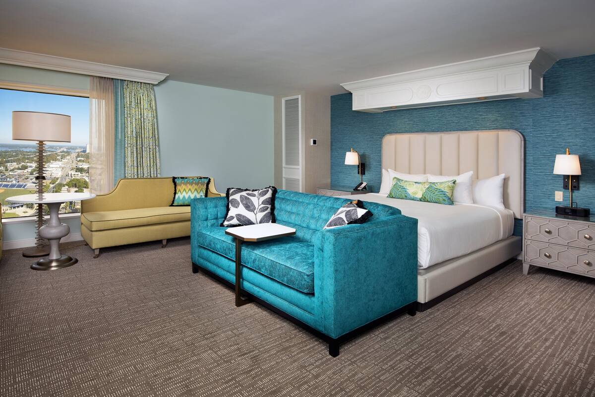 A hotel room with a bed, a sofa, a small table, and a nightstand.