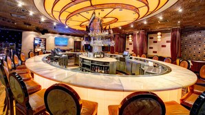 Un espace bar doté d’un bar circulaire, de plusieurs types d’aménagements pour s’asseoir et d’un plafond décoratif.