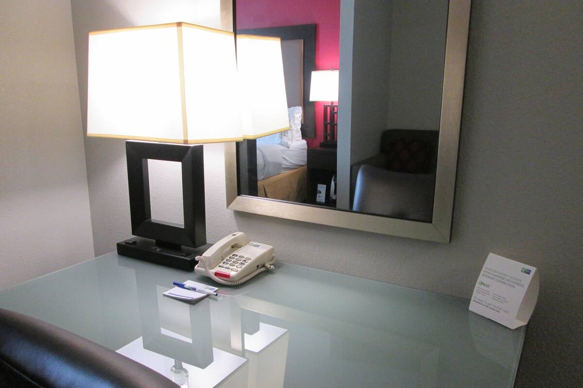 A hotel room with a desk, a telephone, a lamp, a mirror, and a sign indicating high-speed internet access.