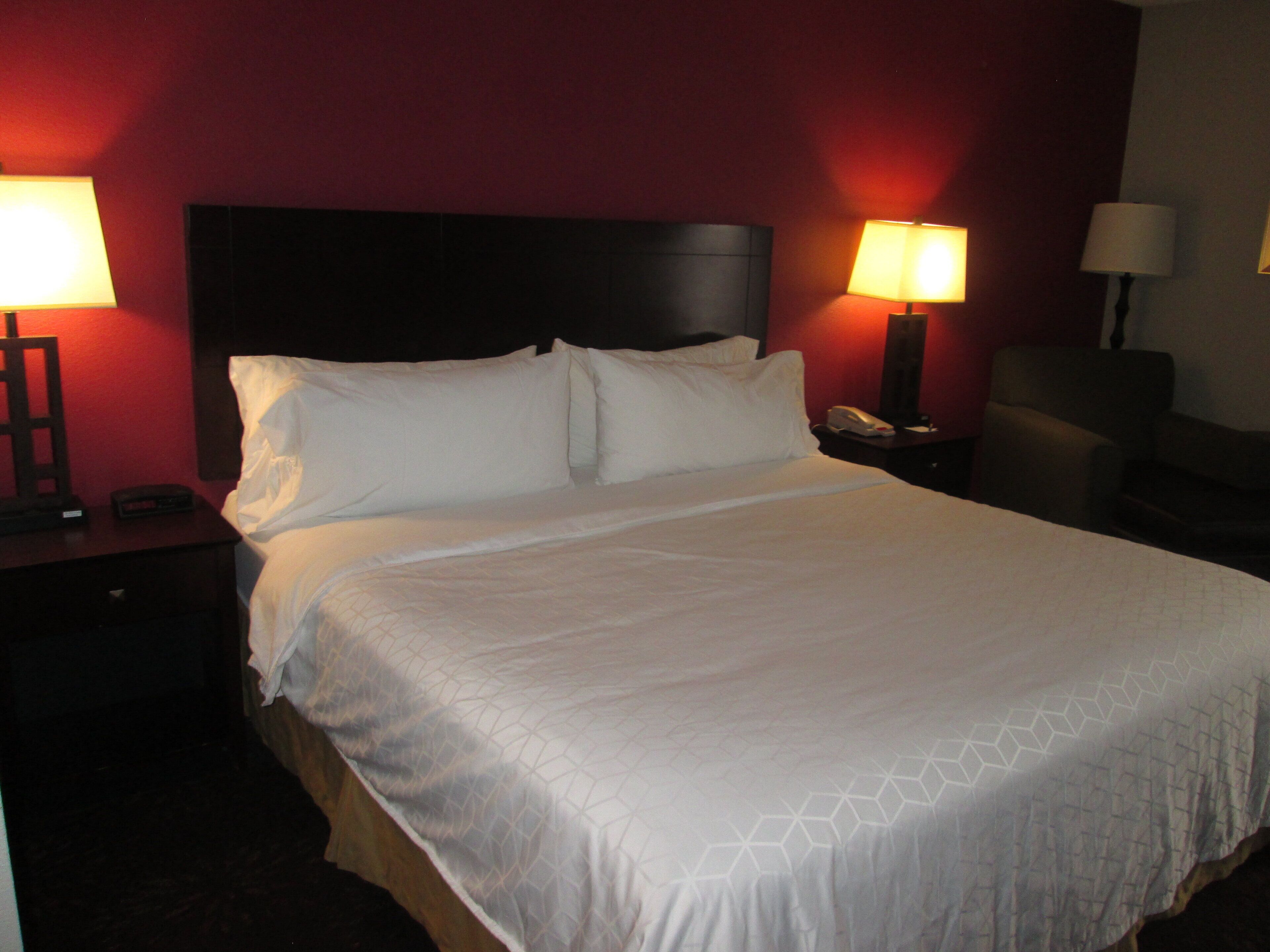 Una habitación de hotel con una cama grande, dos lámparas de noche, una mesita de noche y una silla.