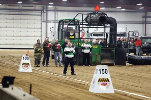 A group of people in a large indoor space with industrial equipment, including a green machine and a truck.