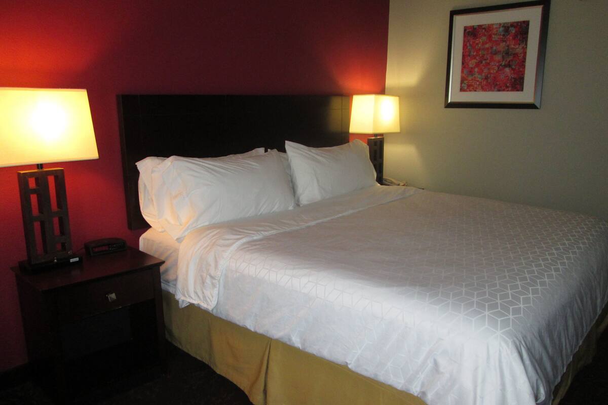 A hotel room with a bed, two bedside lamps, a nightstand, and a framed picture on the wall.